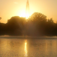 Photo Of Fountain in Pond with Sun Setting Over Trees